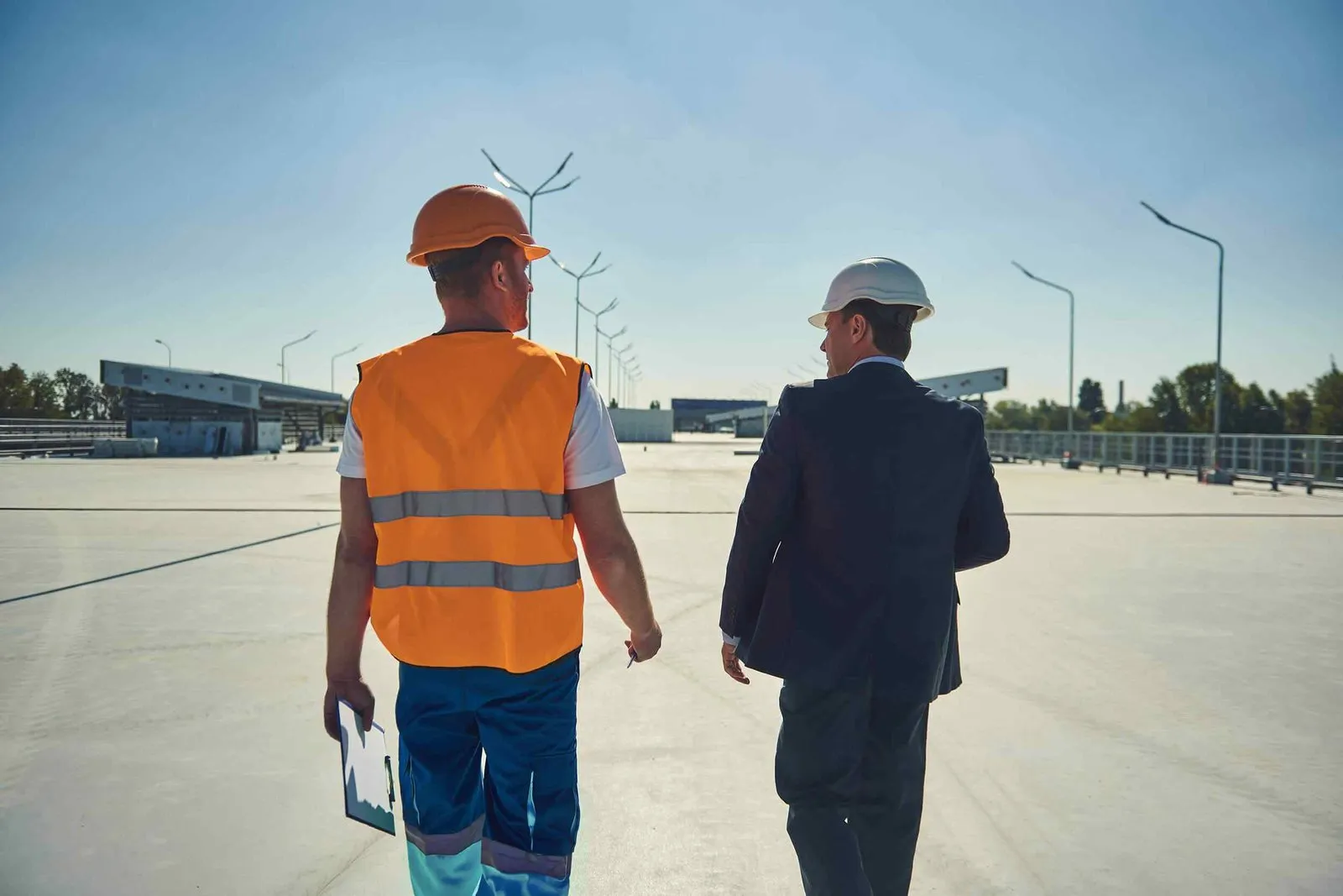 Mitarbeiter in Warnweste und Bauherr gehen gemeinsam über eine Baustelle