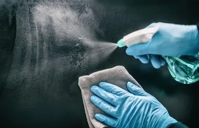 Hand in Schutzhandschuh reinigt eine Oberfläche mit Sprühflasche und Tuch